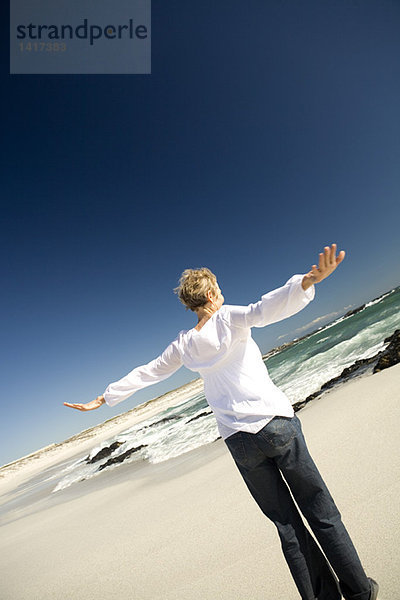 Seniorin mit ausgestreckten Armen am Strand