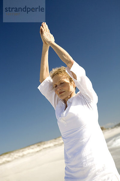 Seniorin beim Yoga am Strand