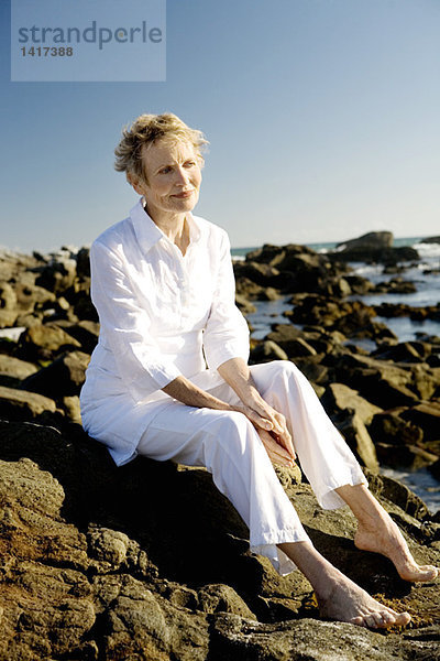Seniorin auf Felsen am Meer sitzend