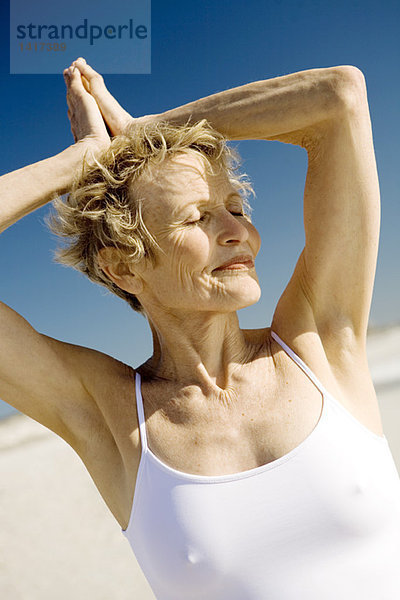 Seniorin beim Yoga am Strand