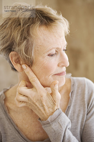 Porträt einer älteren Frau  die ihr Ohr berührt.
