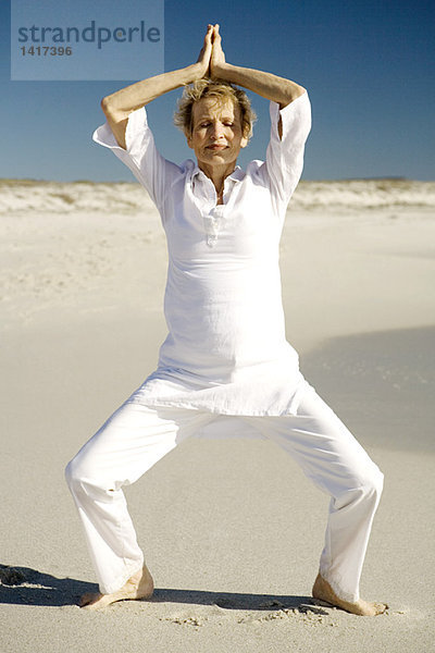 Seniorin beim Yoga am Strand