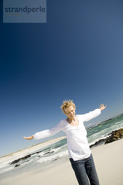 Seniorin mit ausgestreckten Armen am Strand