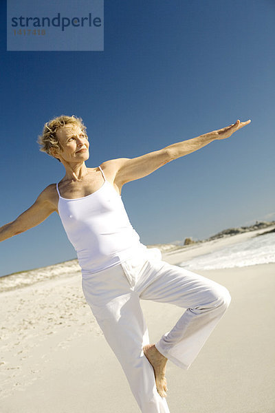 Seniorin beim Yoga am Strand