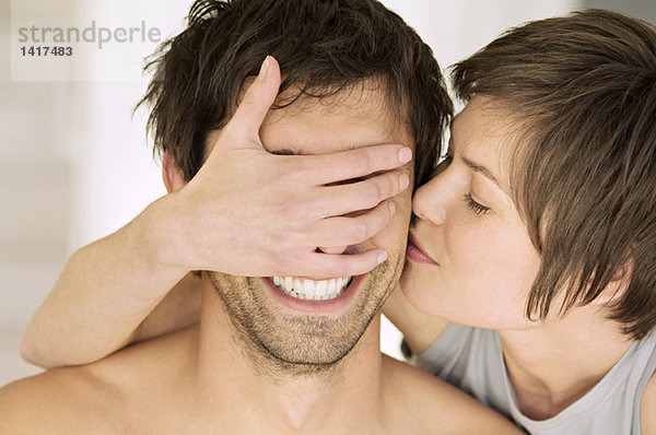 Porträt einer jungen Frau  die den Mann küsst und seine Augen bedeckt.