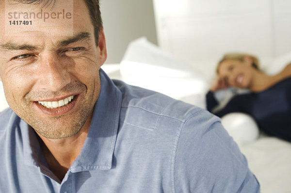 Porträt eines lächelnden Mannes  Frau auf dem Bett liegend im Hintergrund