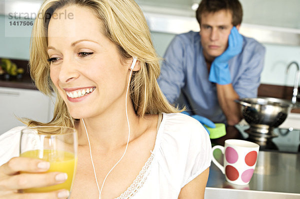 Porträt einer jungen lächelnden Frau mit einem Glas Orangensaft  müder Mann im Hintergrund