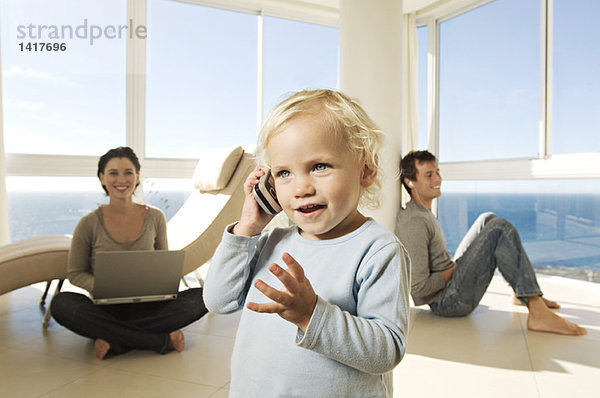 Kleines Mädchen mit Handy  Eltern im Hintergrund