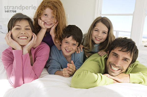 Lächelndes Paar mit 3 Kindern auf dem Bett liegend