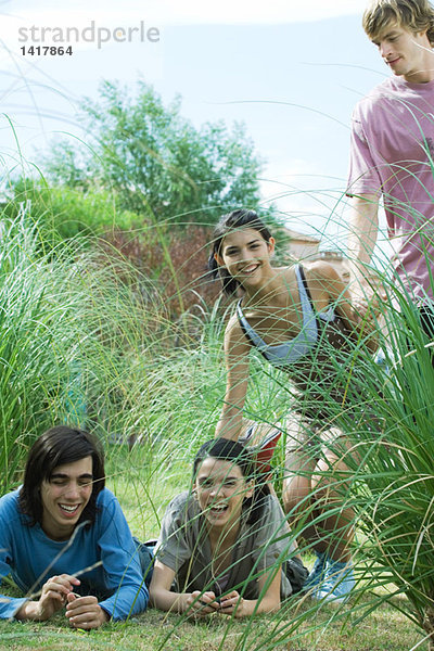 Gruppe junger Freunde  die im Freien lachen  zwei liegen auf Gras.