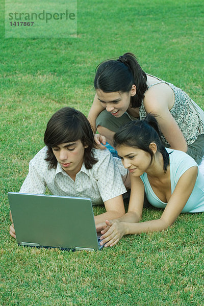 Gruppe junger Freunde im Gras liegend mit Laptop