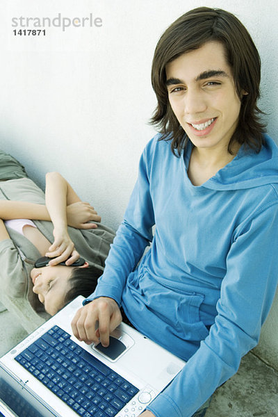 Jugendlicher Junge benutzt Laptop  während weibliche Freundin das Handy benutzt.