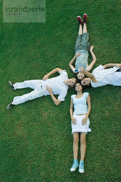 Gruppe junger Freunde auf Gras liegend mit Köpfen zusammen