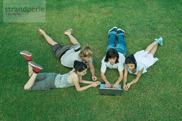 Gruppe junger Freunde auf Rasen liegend  mit Laptop