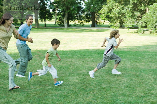 Familie im Freien  die an einem sonnigen Tag über den Rasen läuft.