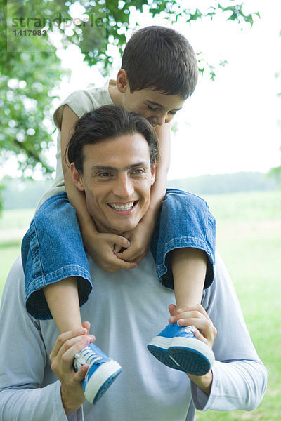 Junge reitet auf Vaters Schultern  beide lächelnd