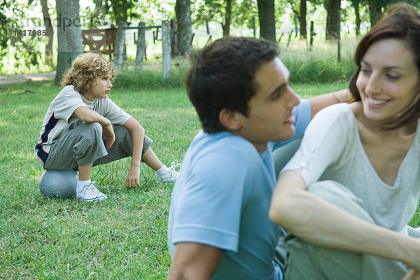 Familie sitzt auf Gras im Freien  Fokus auf Junge sitzt auf Ball im Hintergrund
