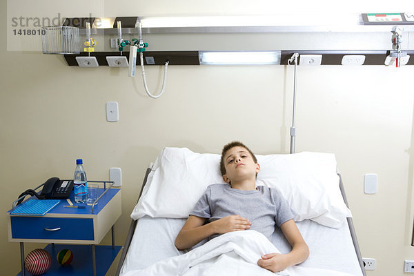 Junge im Krankenhausbett liegend  den Bauch haltend