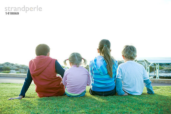 Vier Kinder sitzen auf Gras  Rückansicht