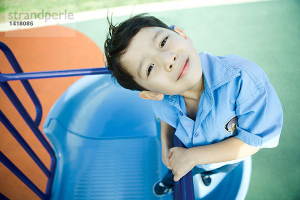 Junge auf Spielplatzgeräten  lächelnd vor der Kamera