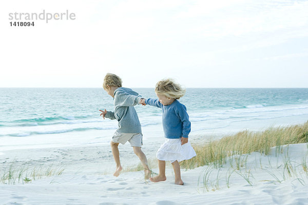 Schwester und Bruder halten Händchen am Strand