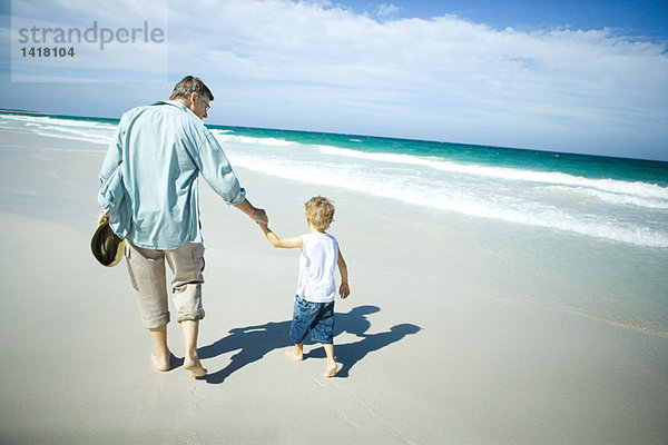 Älterer Mann und Enkel beim Spaziergang am Strand