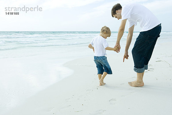 Mann und Sohn am Strand  Mann  der auf Sand zeigt.