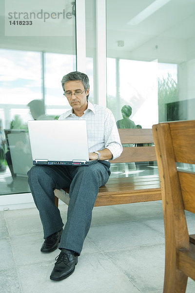 Mann sitzend  mit Laptop auf der Terrasse  volle Länge