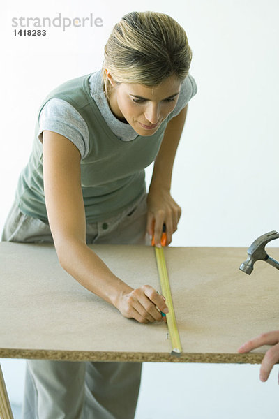 Frau mit Maßband auf Holzbrett zeichnen