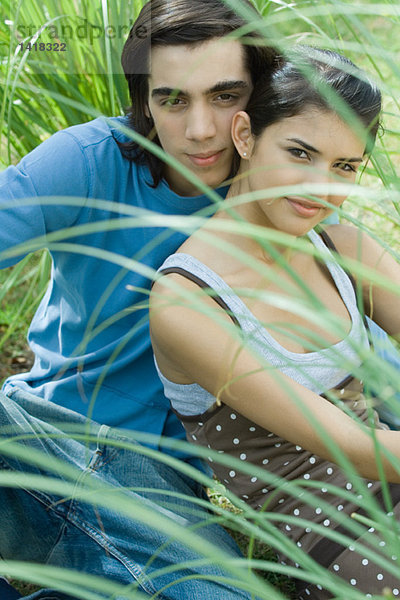 Junges Paar im Gras sitzend  mit Blick auf die Kamera