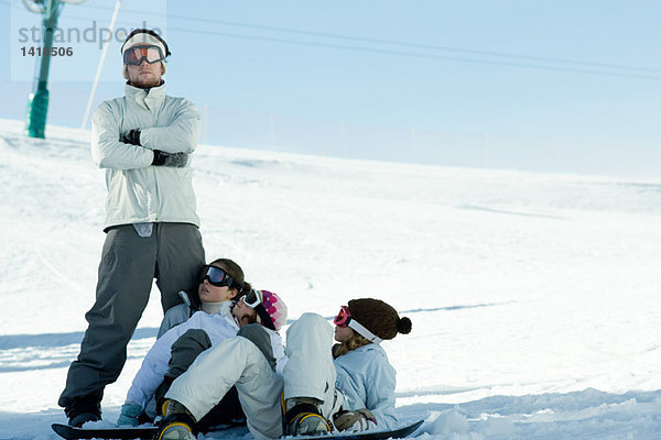 Snowboarder im Schnee liegend  zu einem Freund aufblickend