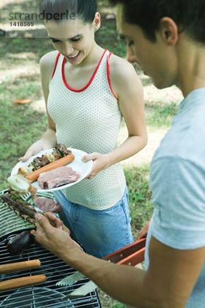 Mann serviert Teenager-Mädchen gegrilltes Fleisch vom Grill
