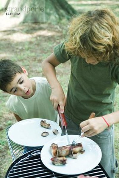 Junge schneidet Fleisch auf dem Teller  während der zweite Junge zusieht.