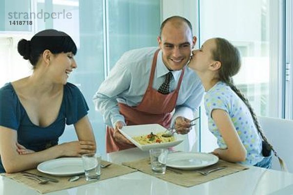 Mann serviert Frau und Tochter Spaghetti  Mädchen küsst Vater auf Wange
