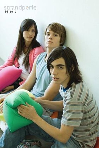 Drei Teenager-Freunde sitzen auf dem Boden und halten Kissen.
