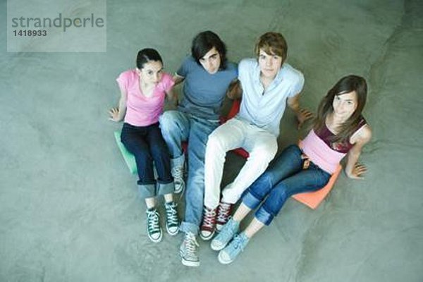 Vier Teenager-Freunde sitzen auf Kissen auf dem Boden  schauen in die Kamera  Hochwinkelansicht