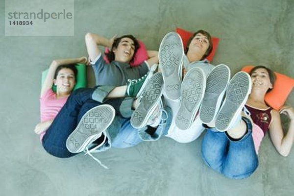 Vier Teenager-Freunde  die auf dem Rücken auf dem Boden liegen  Beine hochhalten  sich auf Schuhsohlen konzentrieren