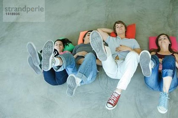 Vier Teenager-Freunde  die auf dem Rücken auf dem Boden liegen  Beine hochhalten  sich auf Schuhsohlen konzentrieren