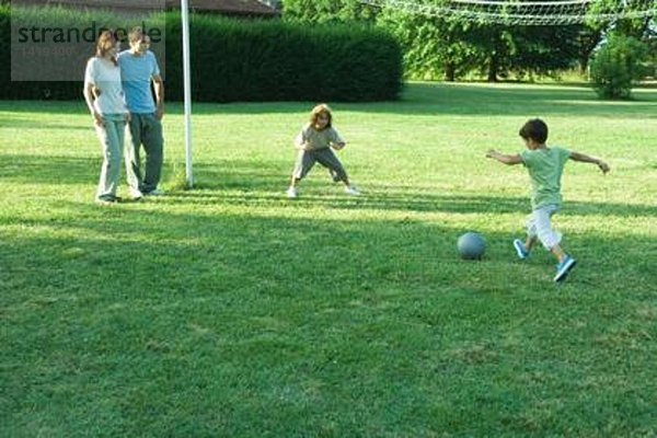 Jungen spielen Fußball  während die Eltern zusehen.