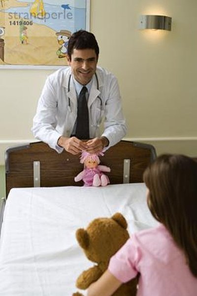 Doktor lächelt kleines Mädchen an  hält Puppe