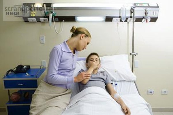 Junge im Krankenhausbett liegend  Mutter sitzend nebeneinander