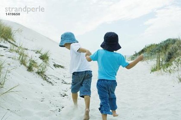 Kinder rennen durch die Dünen und halten sich an den Händen.