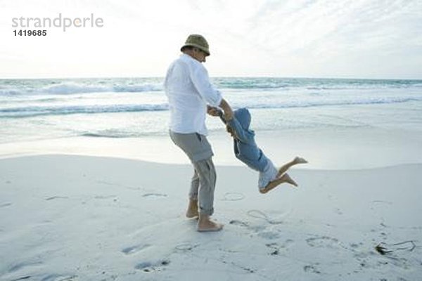 Großvater schwingender Junge am Strand