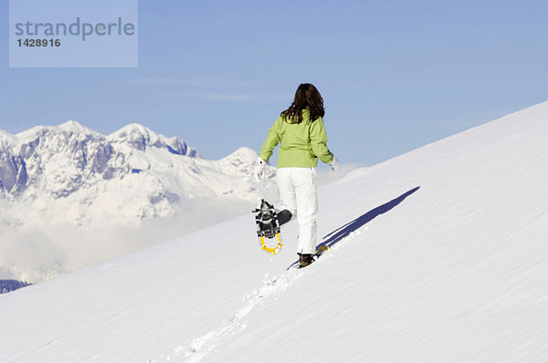 Frau mit Schneeschuhen  die bergauf laufen