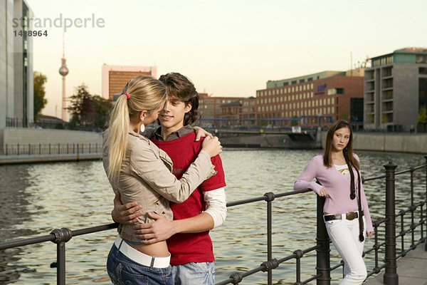 Couple embracing at river  young woman standing in background