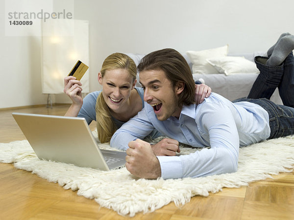 Paar auf dem Boden liegend  mit Laptop