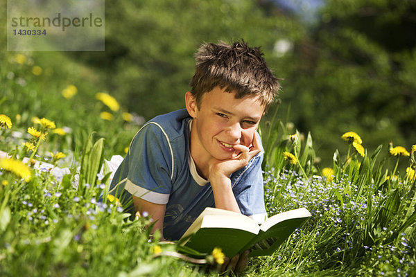 Boy in field reading book  resting head on hand