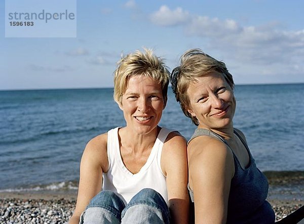 Porträt von zwei Frauen sitzen an einem Strand.