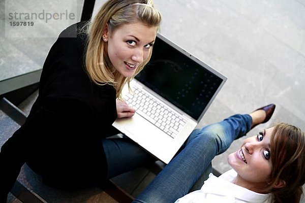 Zwei Frauen sitzen auf der Treppe mit einem Laptop.