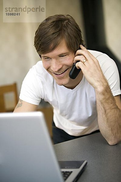 Ein lächelnd mann mit einem Laptop in das Telefon Schweden zu sprechen.